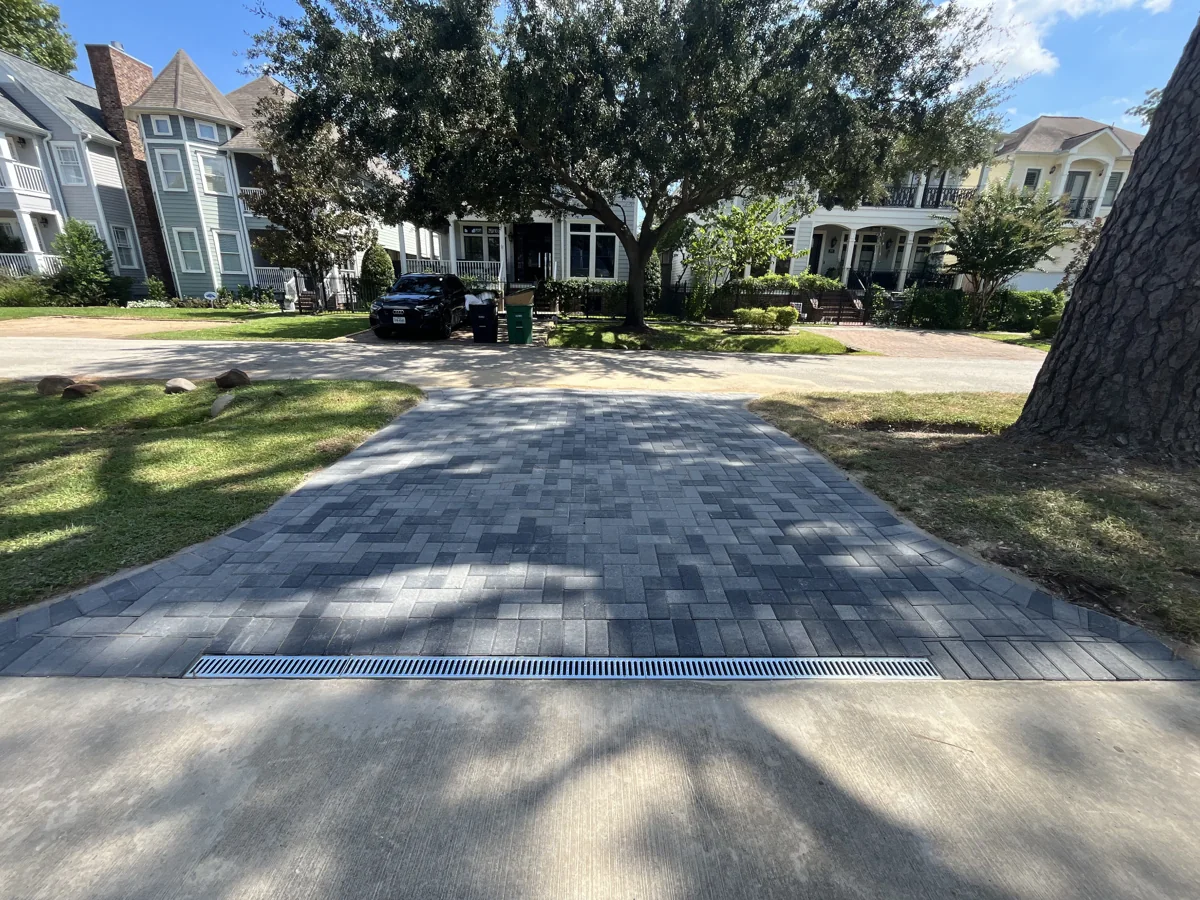 Curved gray paver driveway with a channel drain and mature tree